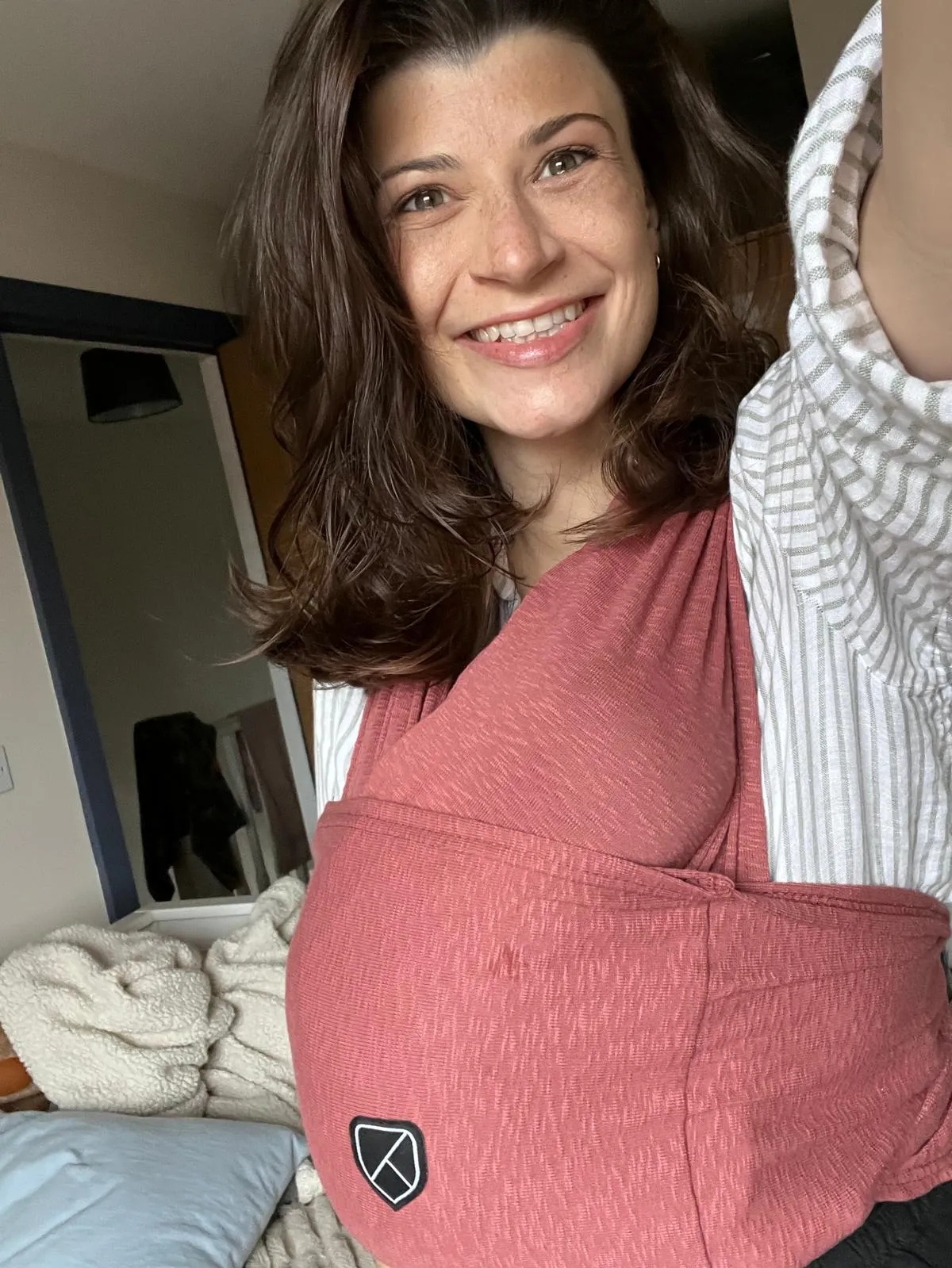 Georgia smiling at the camera with her baby carried in a sling