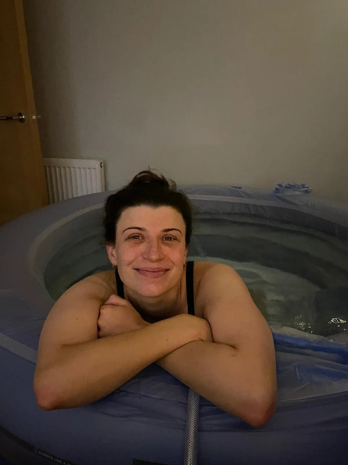 Georgia resting her arms on the edge of a birth pool at home, smiling at the camera